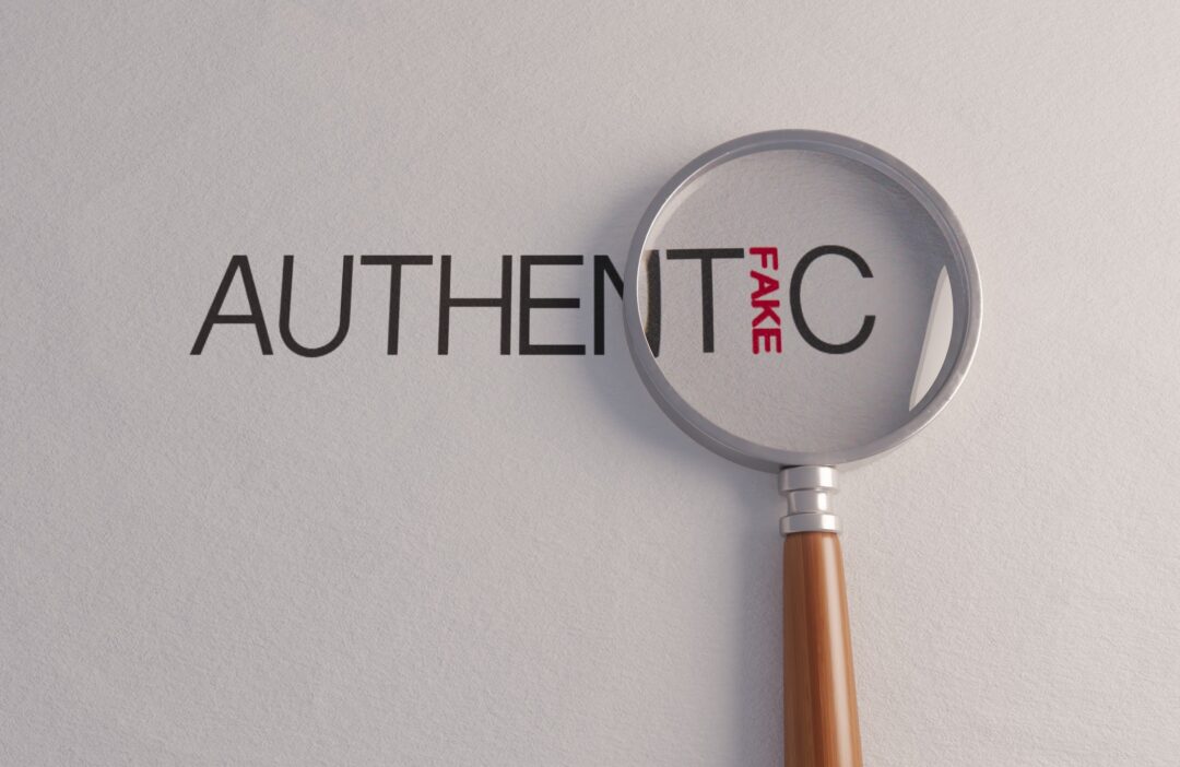 A counterfeit concept of a magnifying glass on white surface showing the word fake hidden in the word authentic