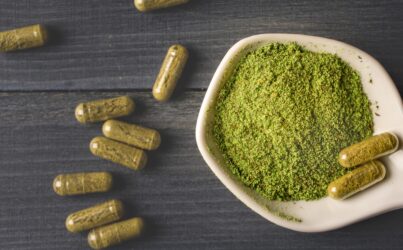 Top view of Kratom powder in ceramic spoon and Kratom capsules on wooden table.