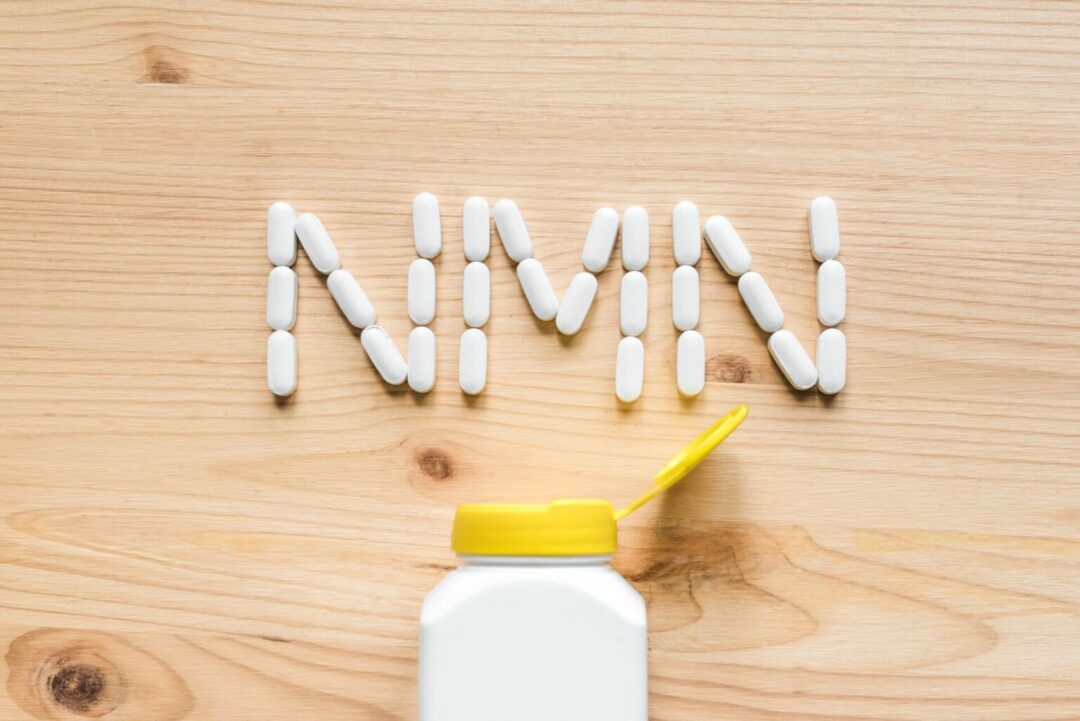 Nicotinamide mononucleotide, niacin, anti adeing vitamin. White pills forming shape to NMN alphabet on wooden background, copy space, top view.