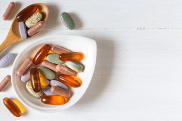 Variety of vitamin pills on white wooden background, supplemental and healthcare product, flat lay surface