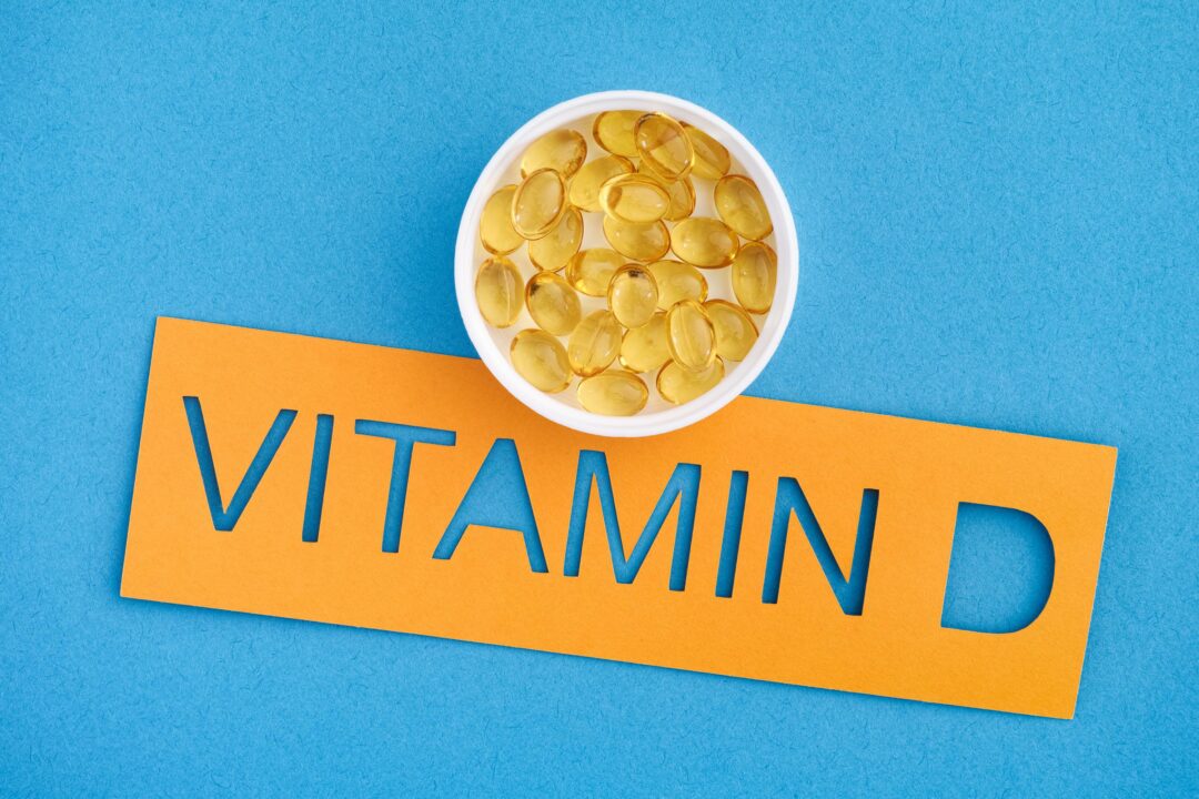 The word Vitamin D with a small cup of Vitamin D3 capsules on it. Close up.