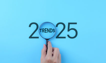 A hand holds a magnifying glass focusing on the word "Trends" within the year "2025." 