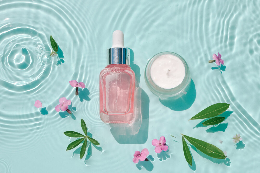 Set moisturizing cosmetic products on water with drops. Serum glass bottle and cream jar on aqua surface with waves in sunlight. Concept for advertising organic moisturizing skin care, spa.