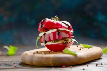 Caprese salad - slices of tomato, mozzarella, basil, pesto and balsamic sauce. Italian homemade food and the concept of healthy eating.