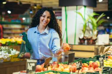 Healthy Lifestyle. Young beautiful Latin American girl chooses and buys apples in the supermarket, puts fruit in an eco bag.