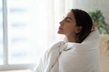 Calm woman wrapped in blanket relax breathing fresh air at home, rest meditate, indoors, stress free concept