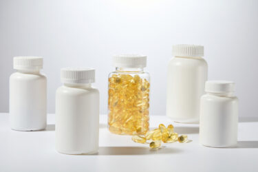 Several medicine bottles mockup neatly standing on the countertop, a transparent bottle of yellow supplement tablets featured in the center, on white background. Front angle shot, space for text