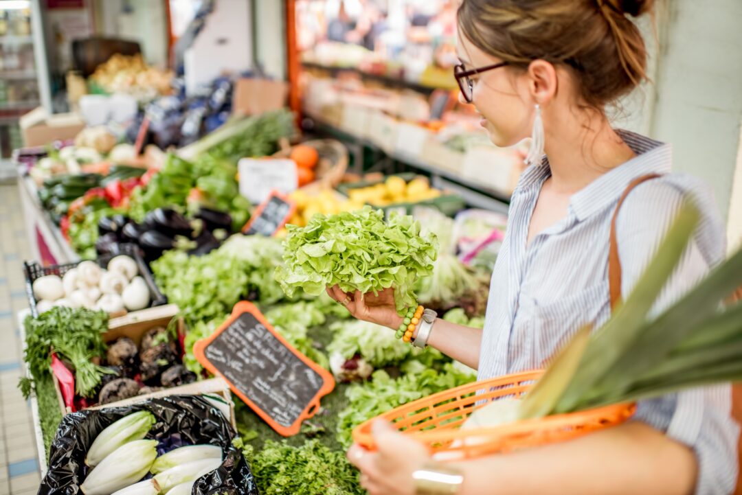 Young woman choosing a fresh salad standing with basket at the food market.