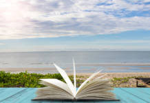 Open book on blue wooden plank with sea beach background