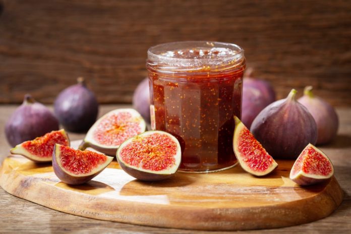 glass jar of figs jam with fresh fruits on wooden table