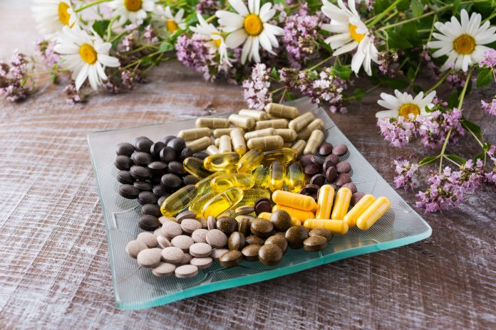 Ayurvedic herbal pills on the glass plate with wild chamomile and tansy flowers. Healthy life concept