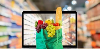supermarket aisle blurred background with laptop computer and green shopping bag on wood table grocery online concept what's selling