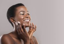 Face lifting concept. Happy black woman with closed eyes touching soft smooth skin on her cheeks over grey background, panorama