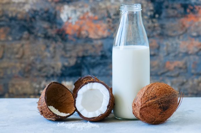 Whole coconuts and coconut products as milk and powder. White stone background.