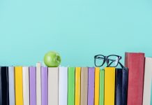 row of books with apple and glasses isolated on blue