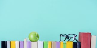 row of books with apple and glasses isolated on blue
