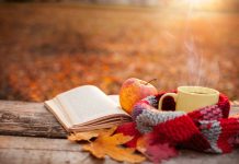 Tea mug with warm scarf open book and apple on wooden surface