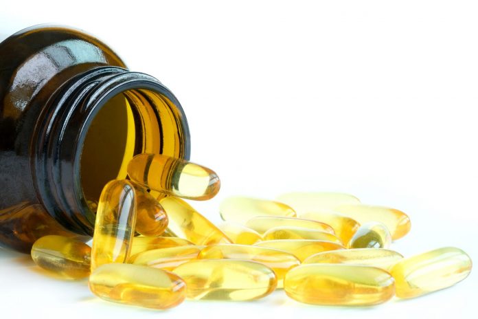 bottle of omega-3 capsules on its side with capsules spilling out on white background