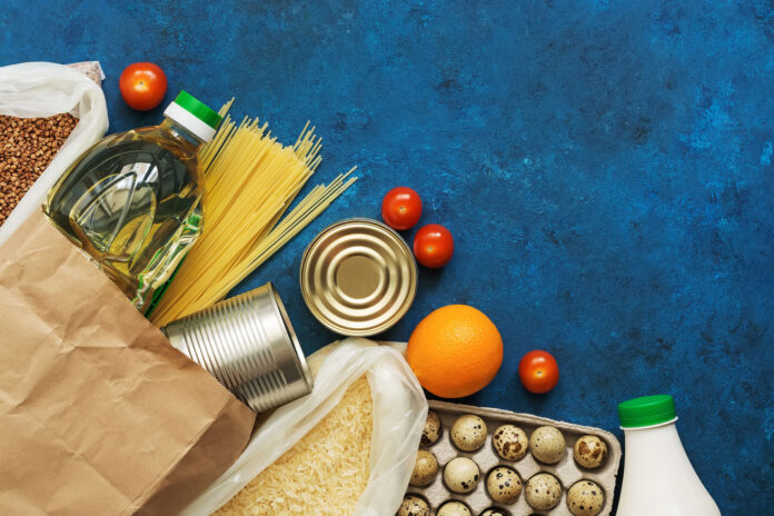Food Home Delivery. Oil in a bottle, pasta, canned food, cereals, eggs, milk, fruits and vegetables on a blue rustic background. Donation and charity. Top view, flat lay,copy space