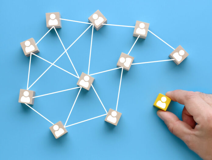 Building a team. Joining a team. Wooden cubes with people icon on blue background. Social network, leadership, team building concepts. Hand moves a wooden block to the group of blocks.