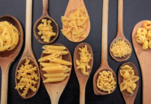 Various shapes of pasta on ladles, black background