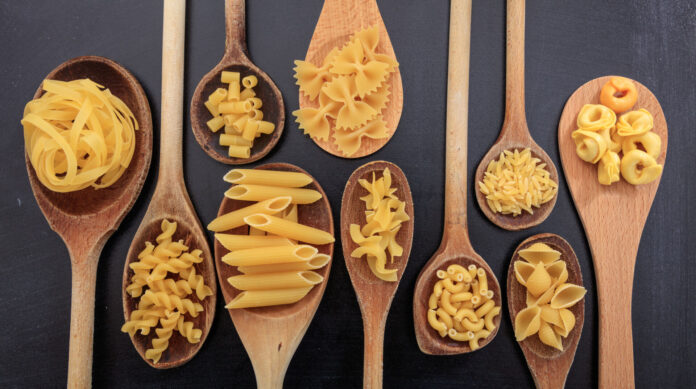 Various shapes of pasta on ladles, black background