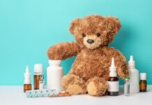 Medicines for children. Teddy bear and bottles with medicines, sprays, syrups, pills on green background.